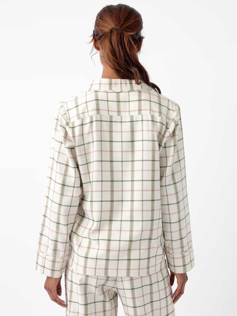A person with reddish-brown hair tied in a ponytail is seen from behind, wearing the Women's Farmhouse Long Sleeve Pajama Set by Cozy Earth. The pajama set has a white plaid design with green and red stripes, and the background is plain white. |Color:Alabaster/Juniper