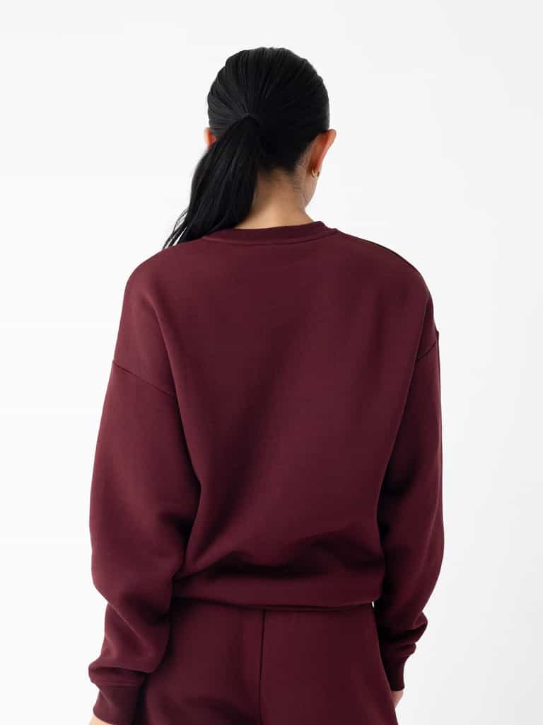 A person with long black hair is shown from the back, wearing a maroon Cozy Earth Women's CityScape Crewneck and maroon pants. The background is plain white. |Color:Burgundy