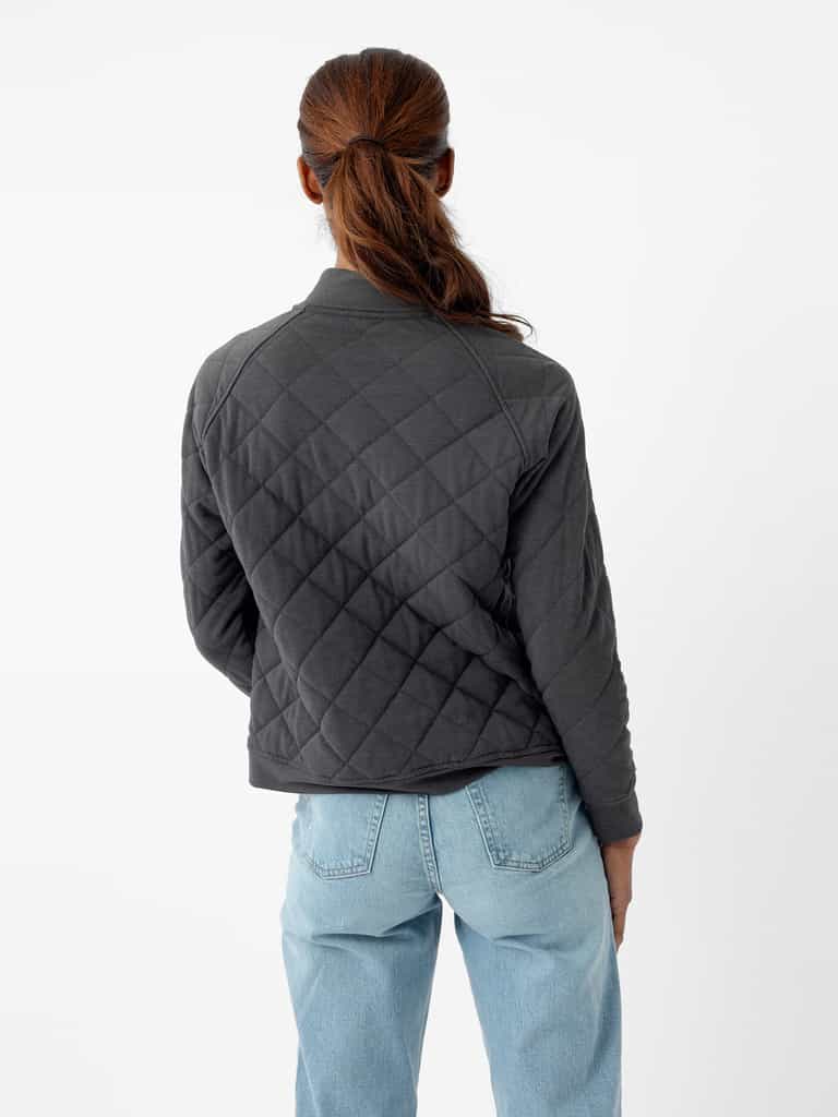 A person with long brown hair tied in a low ponytail is shown from the back. They are wearing a dark gray Women's Ultra-Soft Bamboo Quilted Snap Pullover by Cozy Earth and light blue jeans. The background is plain white. |Color:Charcoal