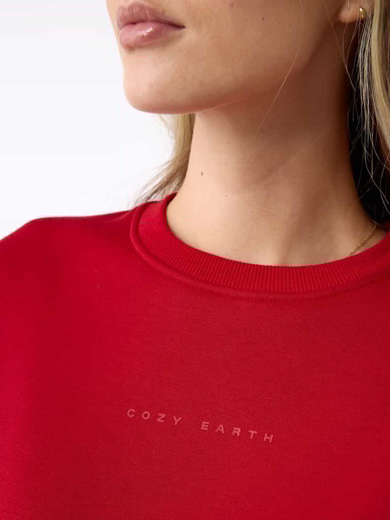 Close-up of a person wearing a red Women's CityScape Crewneck by Cozy Earth. The focus is on the neck and shoulders, showing minimal facial features against a plain white background. |Color:Crimson
