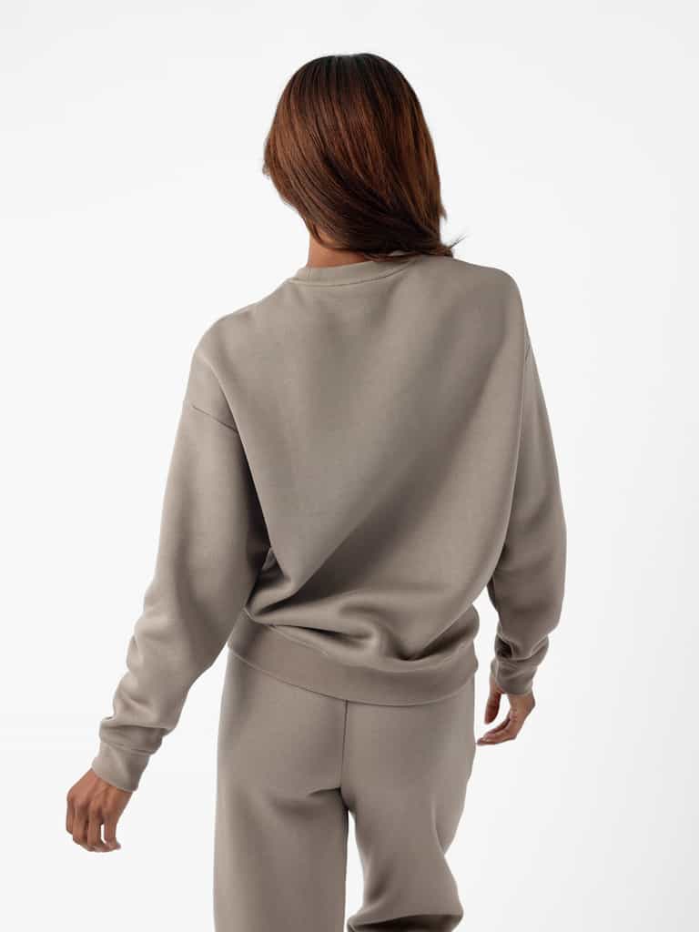 A person with shoulder-length hair is facing away from the camera, wearing a matching light gray Cozy Earth Women's CityScape Crewneck and sweatpants. The background is plain white. |Color:Ebony