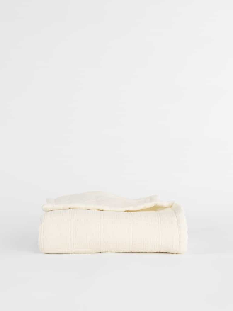A neatly folded Cozy Earth Waffle Windowpane Blanket, available in beige or off-white and featuring a textured grid-like pattern, is placed against a plain white background. |Color:Creme