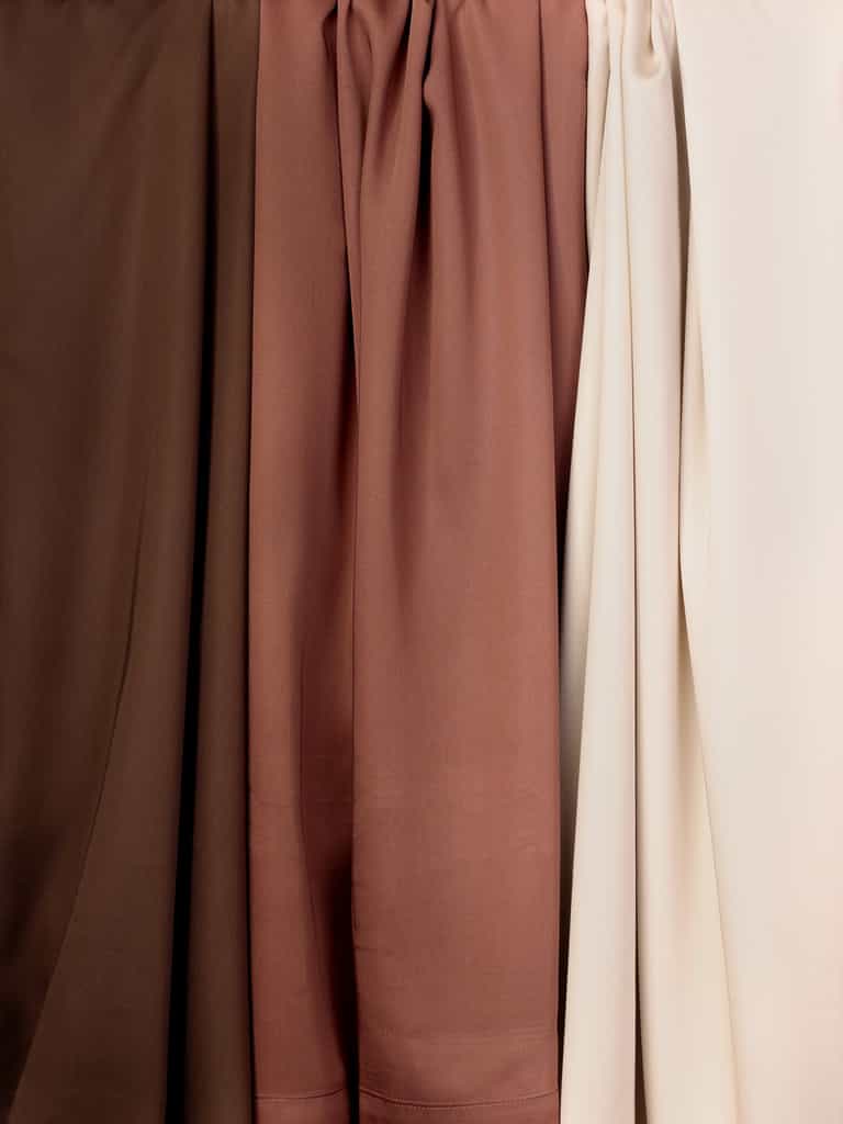 A close-up of four Cozy Earth Bamboo Flat Sheets draped in varying shades of brown and beige. The smooth textures and gentle folds of the sheets create a subtle gradient from dark brown on the left to light beige on the right. |Color:Coffee