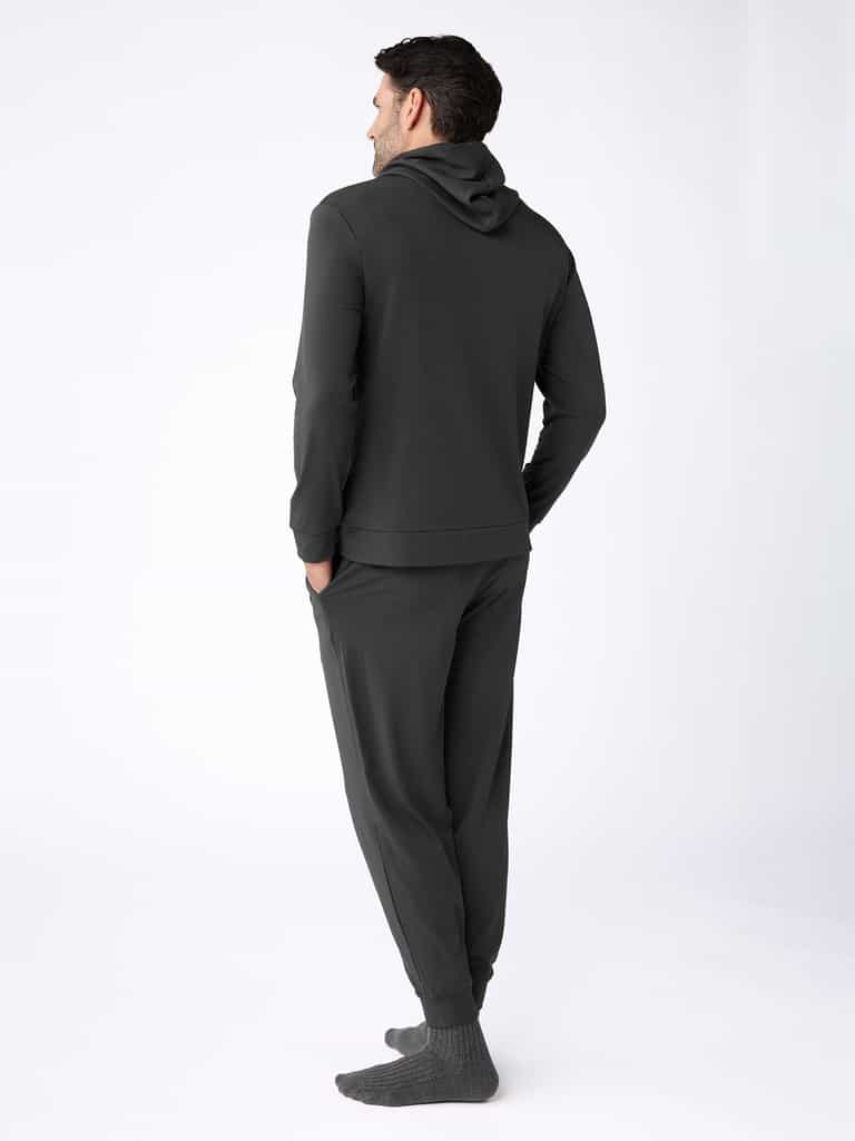 A man faces away, wearing the Cozy Earth Men's Brushed Bamboo Hoodie & Jogger Set with gray socks against a plain, light background. |Color:Charcoal