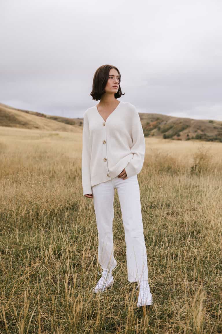 A woman wearing Cozy Earth Classic Cardigan in white stands in a field |Color:Ivory