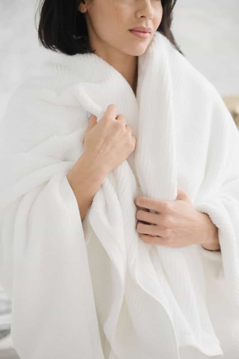 Ribbed Terry Bath Sheets in the color White. Photo of product taken in a bathroom as a woman wears the towel. |Color:White