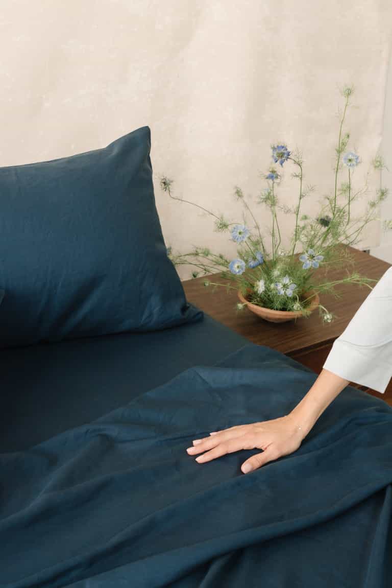 Navy Bamboo Linen Pillow Cases on a bed. A woman is running her hands along the bed. |Color: Navy