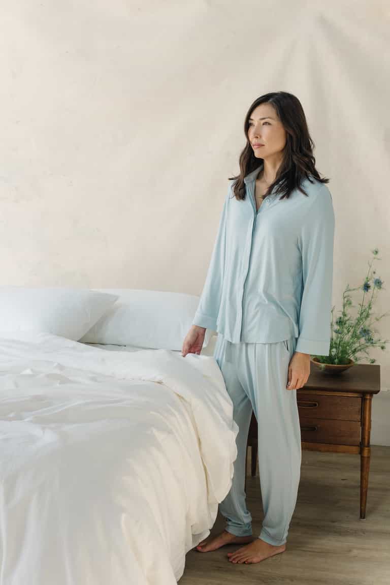 White Bamboo Linen Pillow Cases on a navy bed. A woman in pajamas is standing next to the bed.|Color: White