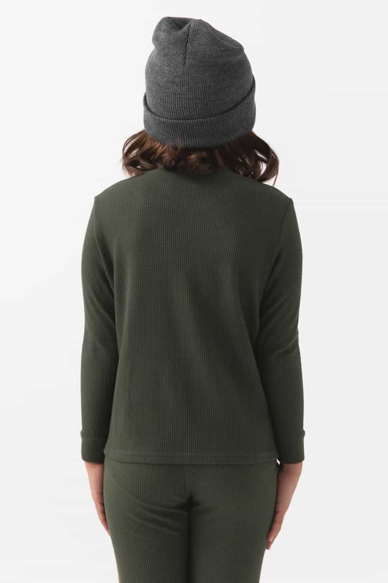 A child faces away from the camera, wearing Cozy Earth's Children's Bamboo Waffle Knit Base Layer Long Sleeve in dark green, with matching pants and a gray knit beanie against a plain white background.|Color:Olive