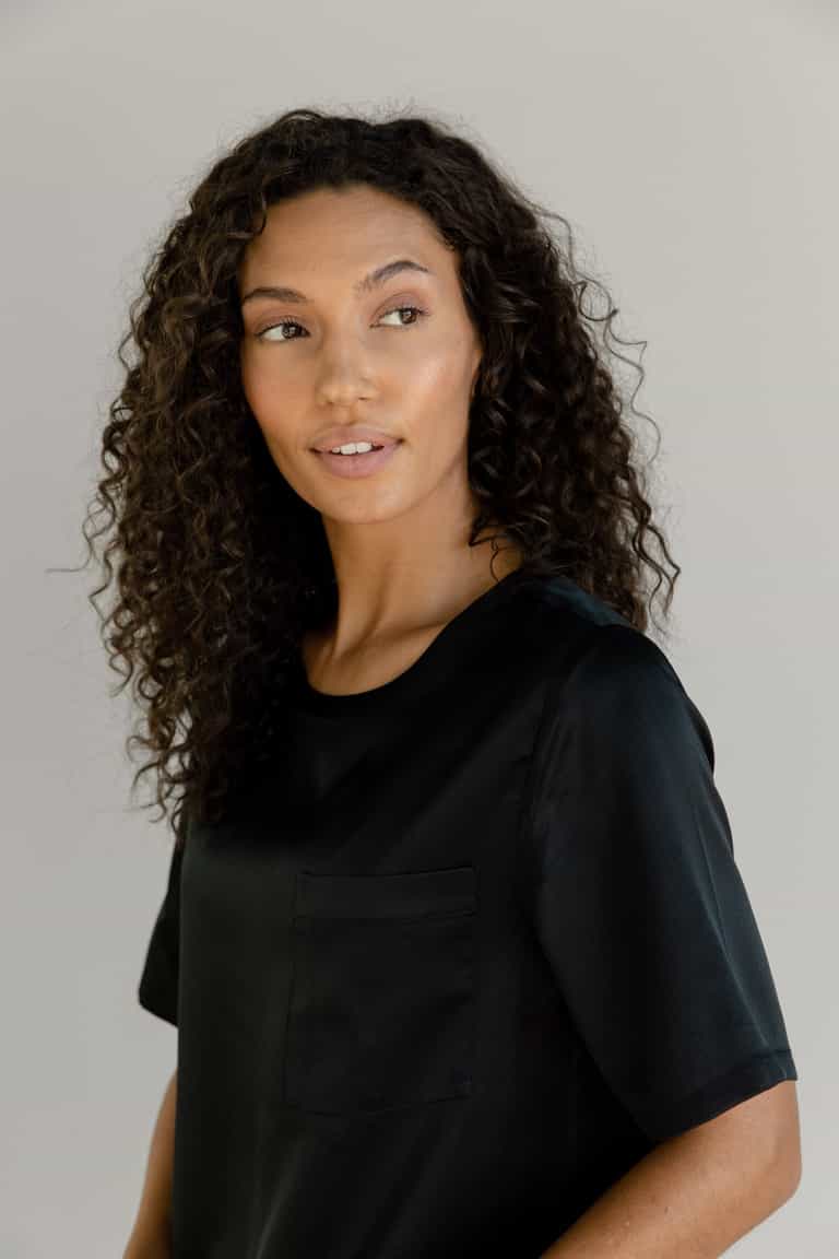 Black Serenity Silk Scoop Neck Tee modeled by a woman. The photo was taken in a high contrast setting, showing off the colors and lines of the tee. |Color: Black