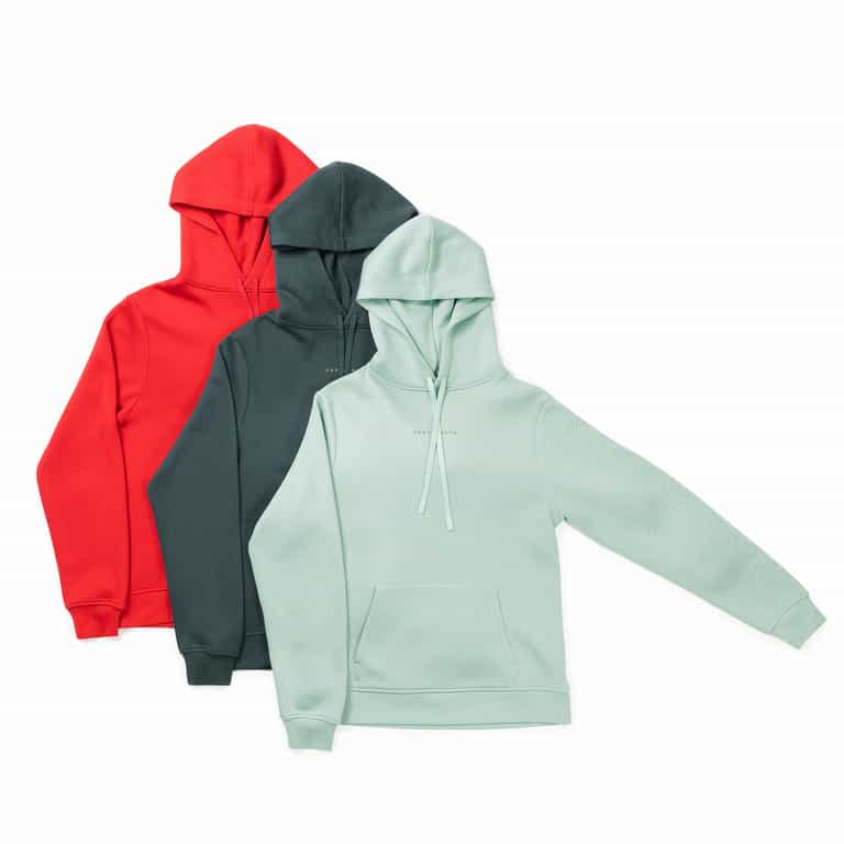 Three **Men's CityScape Hoodies** by **Cozy Earth** are showcased in a staggered arrangement. From left to right, they come in red, dark green, and light mint green colors. Each hoodie features a front pocket and a drawstring hood, with the mint green hoodie positioned in the foreground. |Color:Spruce