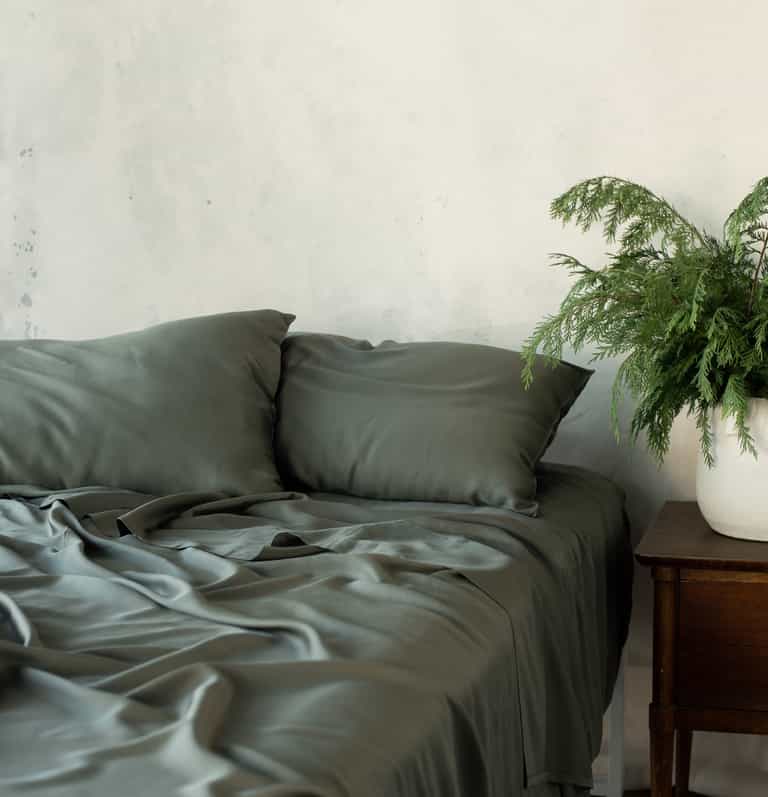 Unmade bed with olive bedding and a plant on the nightstand |Color:Olive