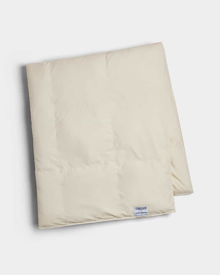 The Cozy Earth Down Alternative Throw is a folded, cream-colored quilt with a small rectangular label near the edge, displayed on a white background.|Color:Coconut