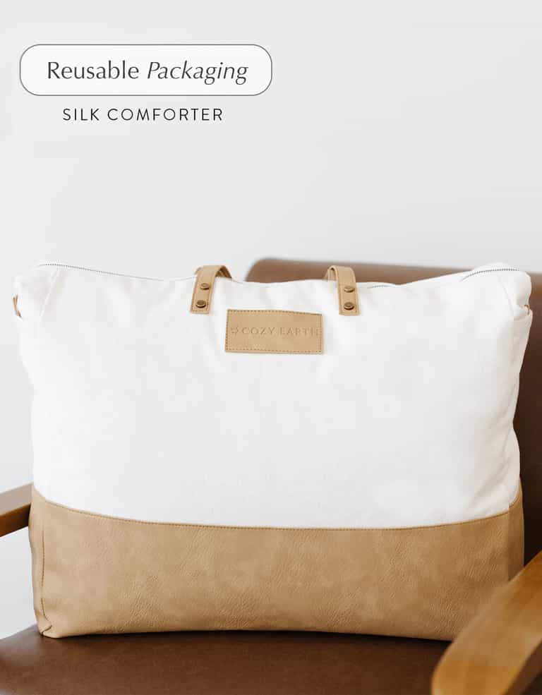 A large beige and white fabric bag labeled "Cozy Earth" with the text "Reusable Packaging, Silk Comforter" sits on a brown chair.|Filling:Standard
