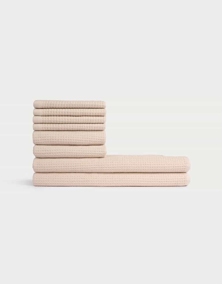 The Cozy Earth Waffle Bath Towel Set features eight neatly folded beige towels with a textured waffle pattern, stacked in two piles against a plain white background. |Color:Birch