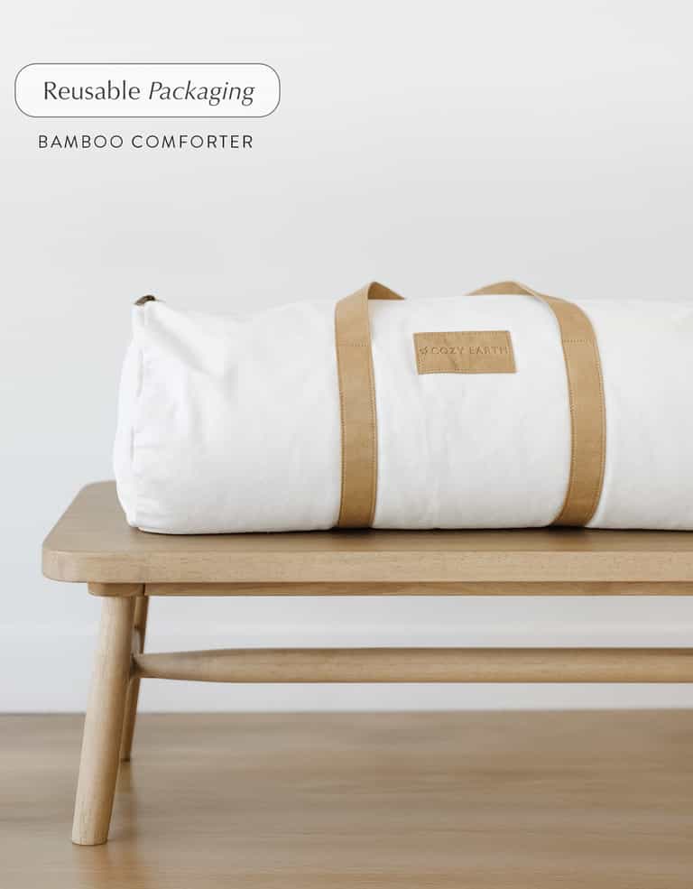 A Cozy Earth Bamboo Viscose Comforter in a reusable duffel bag with tan straps sits on a wooden bench; text reads "Reusable Packaging, Bamboo Viscose Comforter. |Filling:Standard