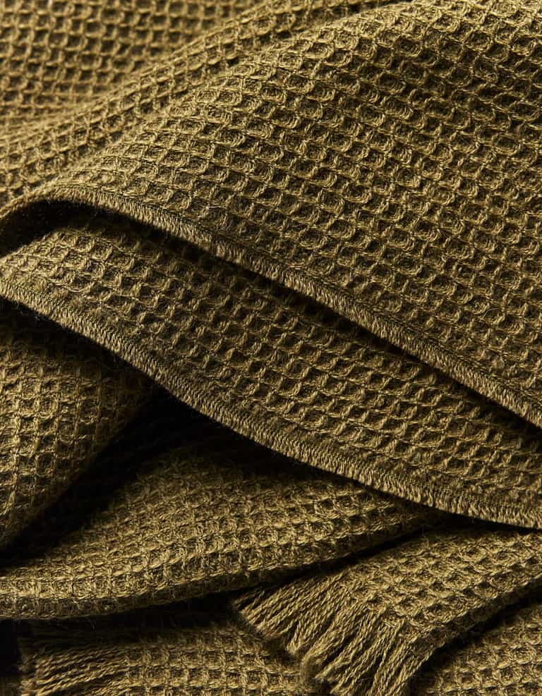 Close-up of the Cozy Earth Alpaca Waffle Throw, showcasing its textured olive green waffle weave, soft folds, and fringed edges.|Color:Utility Green