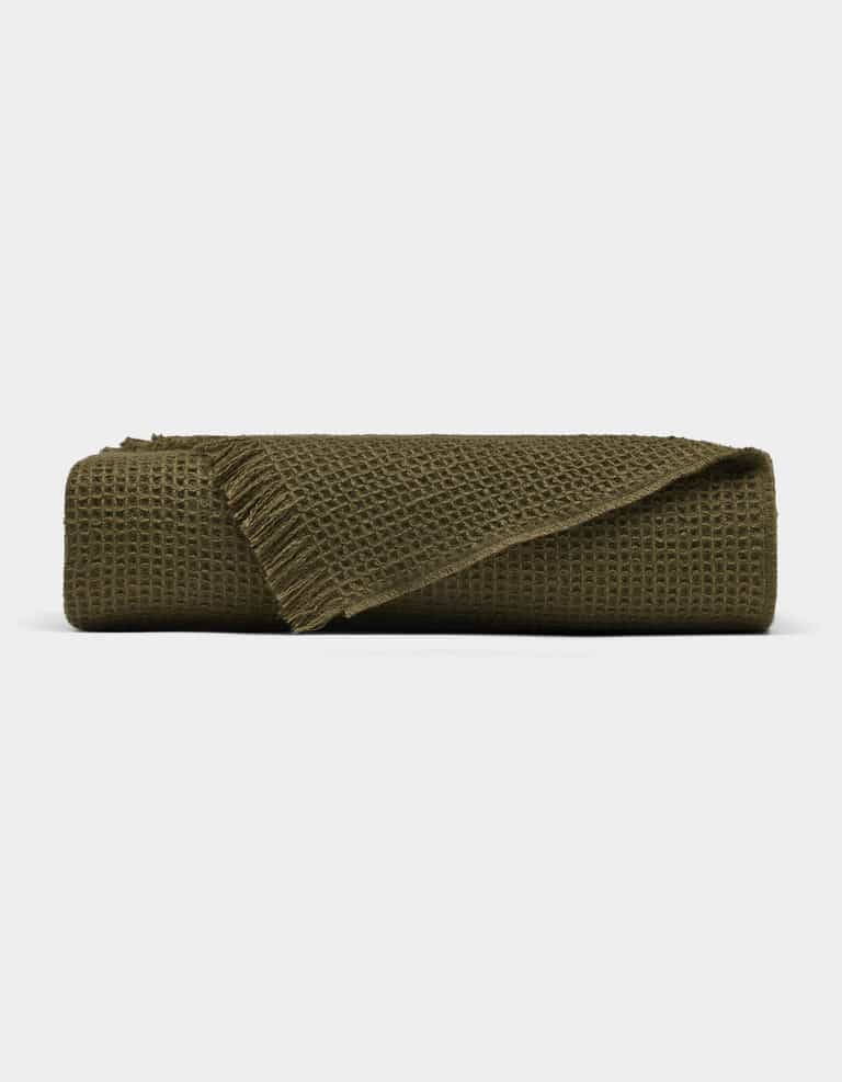 The Cozy Earth Alpaca Waffle Throw, in dark olive green with a waffle texture and fringed edges, is shown folded against a plain white background.|Color:Utility Green