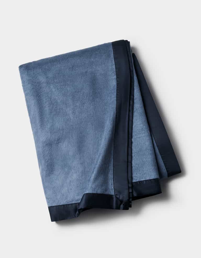 The Cozy Earth Bamboo Blanket, in blue with a dark satin trim, is shown folded against a plain light background.|Color:Pacific Blue/Navy