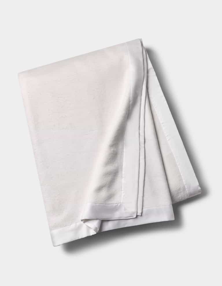 The Cozy Earth Bamboo Blanket, featuring a smooth satin border, is shown folded on a light gray background.|Color:White