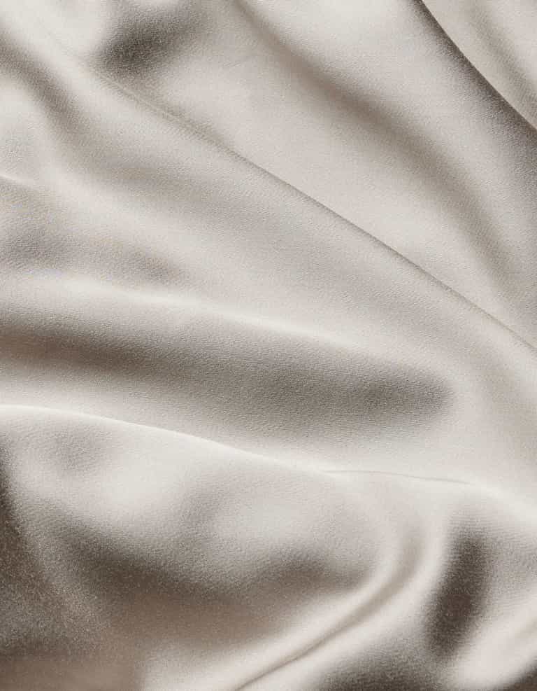 The Bamboo Flat Sheet by Cozy Earth features smooth, cream-colored satin fabric with gentle, flowing folds and a soft sheen that beautifully reflects light.|Color:Dove Grey