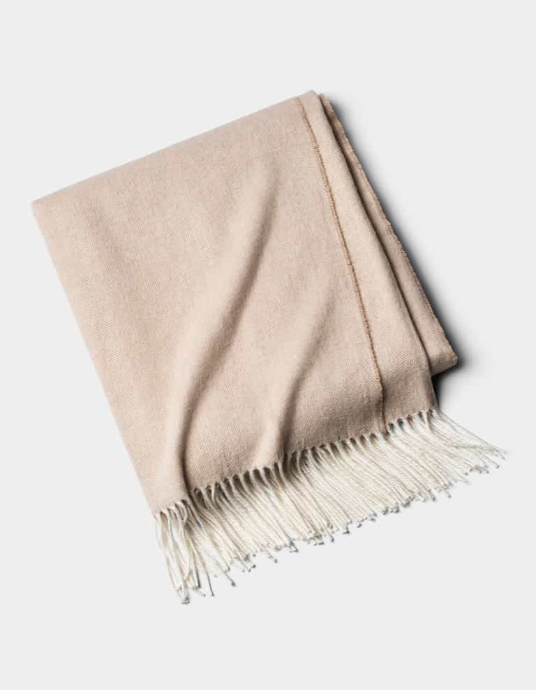 The Cozy Earth Bamboo Herringbone Tassel Throw, a beige blanket with white fringed edges, is shown folded on a plain white background.|Color:Oatmeal