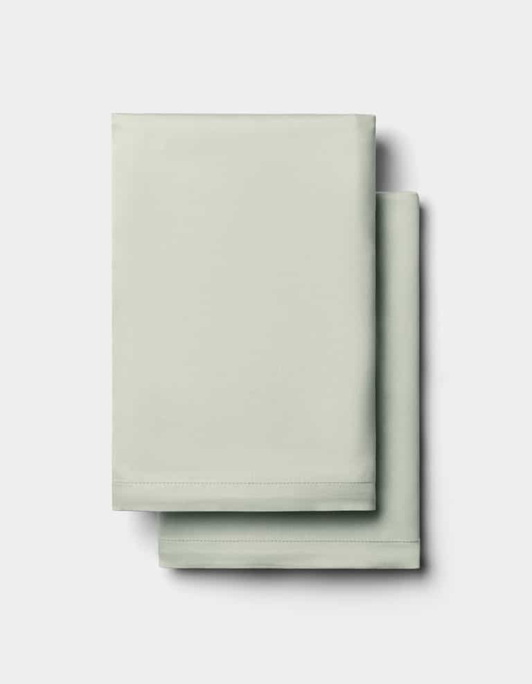 Two neatly folded Cozy Earth Bamboo Pillowcases in light green are stacked on top of each other against a plain white background.|Color:Laurel