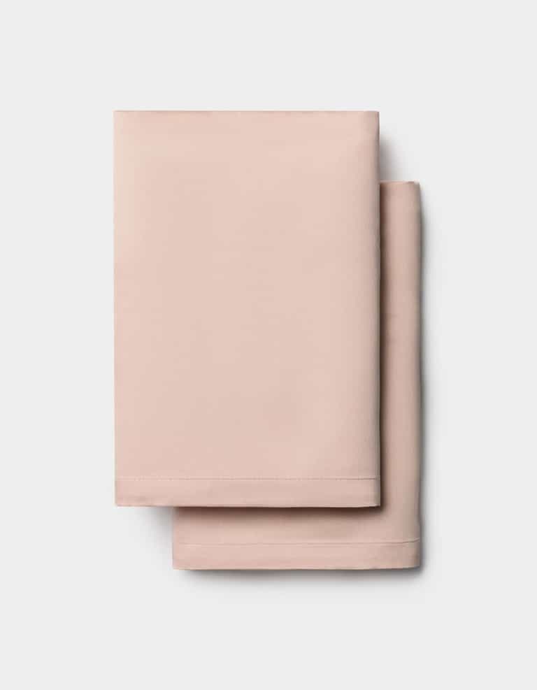 Two neatly folded light pink Cozy Earth Bamboo Pillowcases stacked on a white background.|Color:Peony