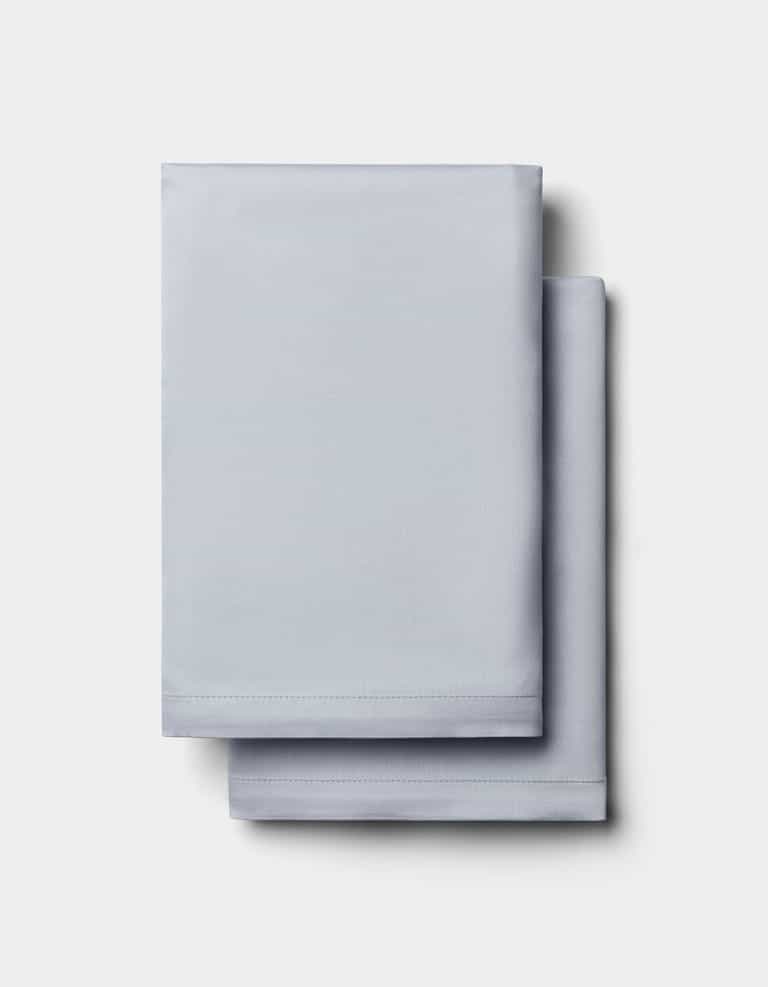 Two neatly folded Cozy Earth Bamboo Pillowcases in light gray are stacked on a plain white background.|Color:Shore