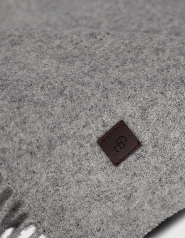 Close-up of Cozy Earth’s Cashmere Tassel Throw in soft light grey, showing its cozy texture. A small brown leather tag with an embossed logo is stitched on for a refined touch.|Color:Pebble