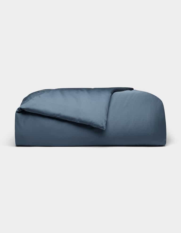 The Cozy Earth Bamboo Duvet Cover, in dark blue and rectangular shape, features plush fabric with a partially folded comforter, displayed against a plain light gray background.|Color:Pacific Blue