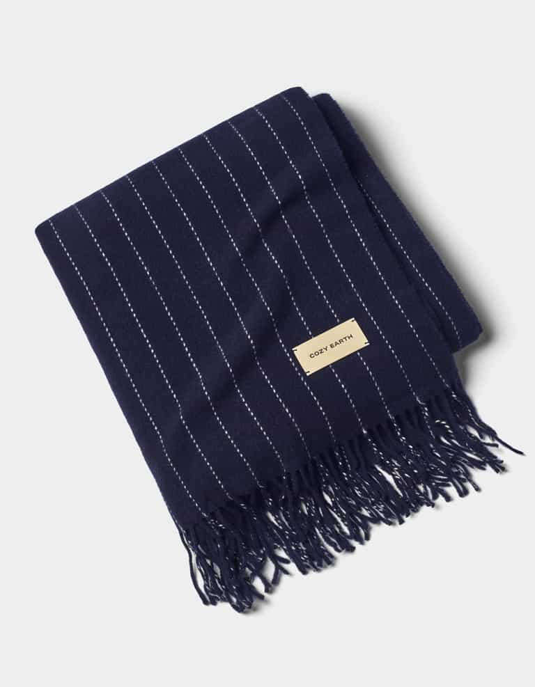 A neatly folded Florence Throw by Cozy Earth, featuring navy blue with thin white vertical stripes, fringed edges, and a beige fabric label on one end, displayed against a light background.|Color:Navy