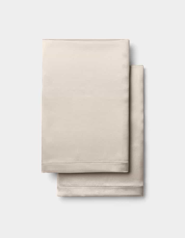 Two neatly folded Cozy Earth Silk Pillowcases in beige, stacked together against a plain white background.|Color:Driftwood