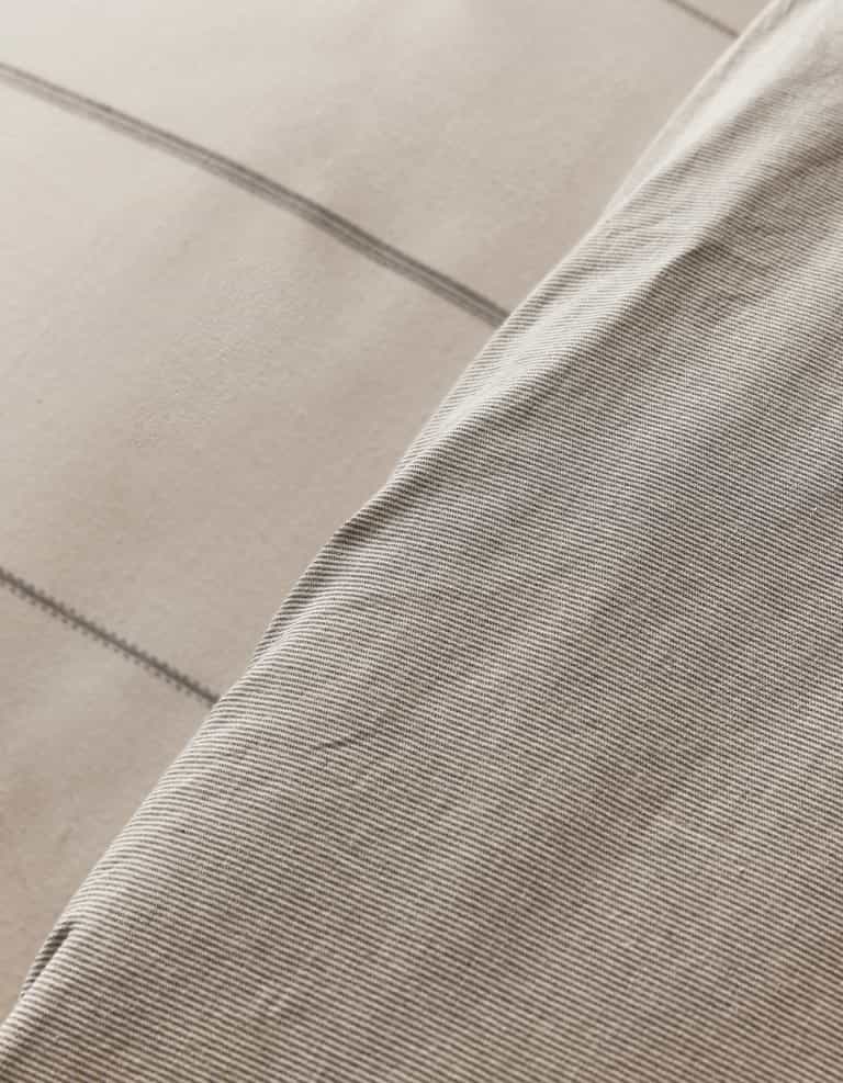 A close-up of the Cozy Earth Baja Duvet Cover shows two overlapping fabrics—one with thin light gray pinstripes, the other with a beige background and wide gray plaid lines. Both textiles feature a soft, woven texture.|Color:Coal Stripe/Striped Alabaster