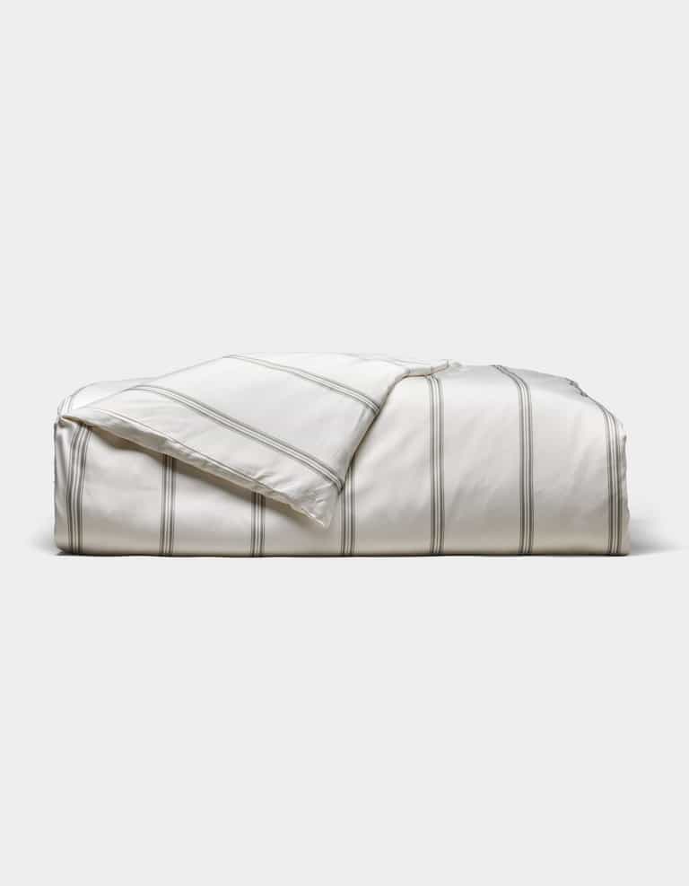 The Cozy Earth Bamboo Duvet Cover, white with thin gray stripes, is neatly folded against a light gray background. A corner is turned down to reveal the underside.|Color:Baja Stripe in Laurel