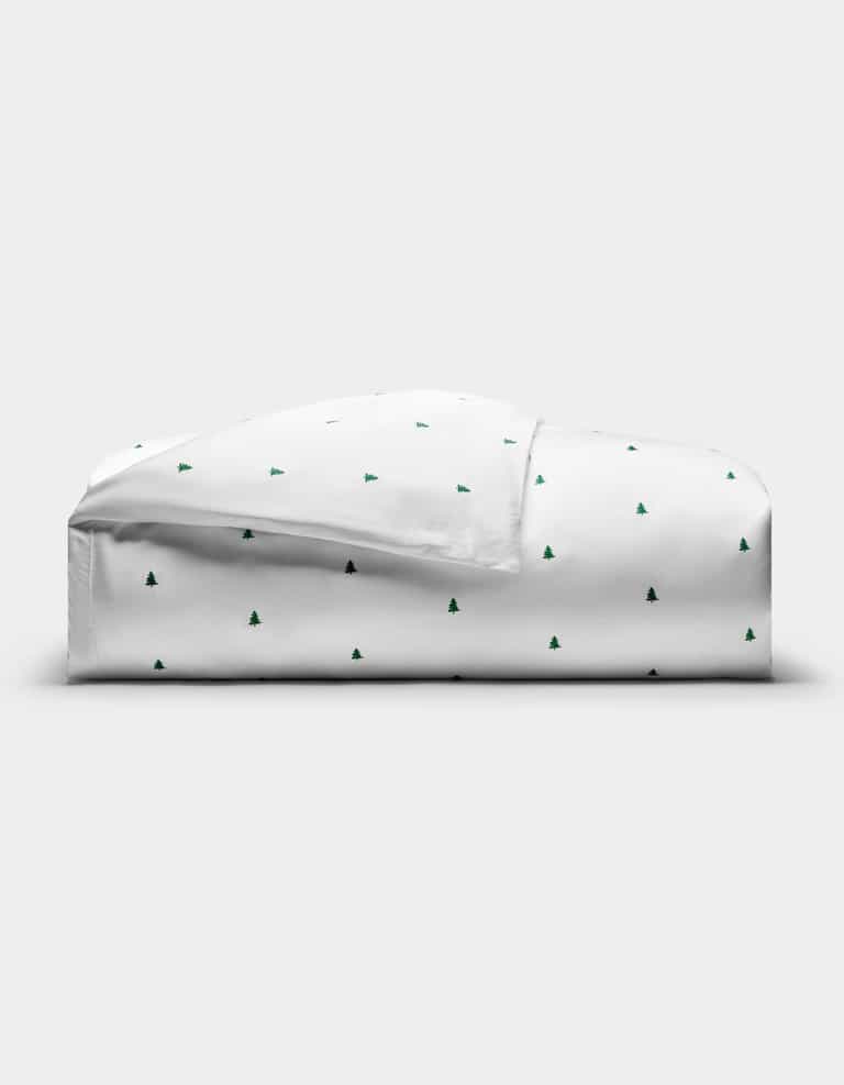 The Cozy Earth Bamboo Duvet Cover, featuring a minimal pattern of small green Christmas trees, is neatly folded on a plain white background.|Color:Jade Tree Snow