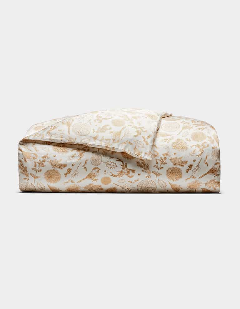 The Bamboo Duvet Cover by Cozy Earth is shown folded, featuring a white background with a gold floral and botanical print of detailed flowers, leaves, and birds, displayed against a plain white background.|Color:Winter Toile Dijon