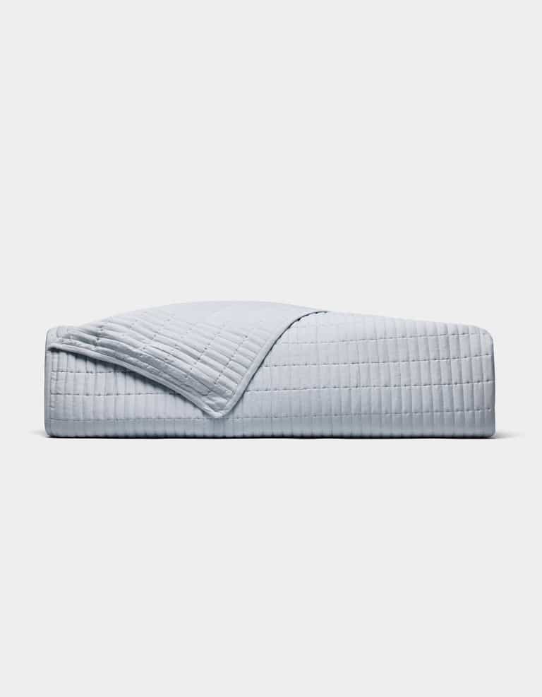 A neatly made bed displays the Cozy Earth Bamboo Jersey Quilt in light grey with a matching pillow, one quilt corner folded back, all set against a plain white background.|Color:Shore