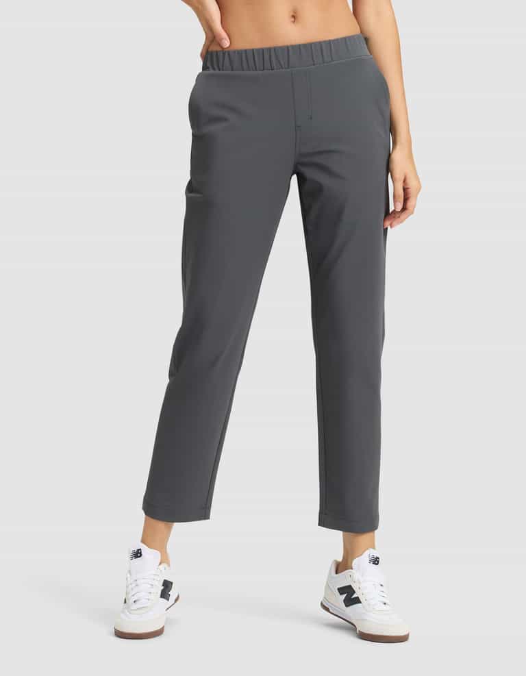 A person wears Cozy Earth’s Women's Always Cropped Pant in dark gray with an elastic waistband, paired with white sneakers featuring blue accents, standing against a plain light background. |Color:Coal