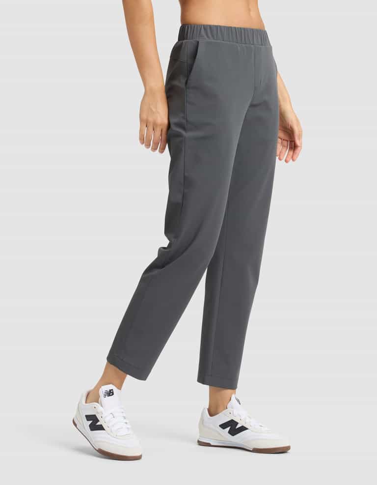 A person wears Cozy Earth's Women's Always Cropped Pant in gray and white New Balance sneakers, standing with one hand in their pocket against a plain light background. |Color:Coal