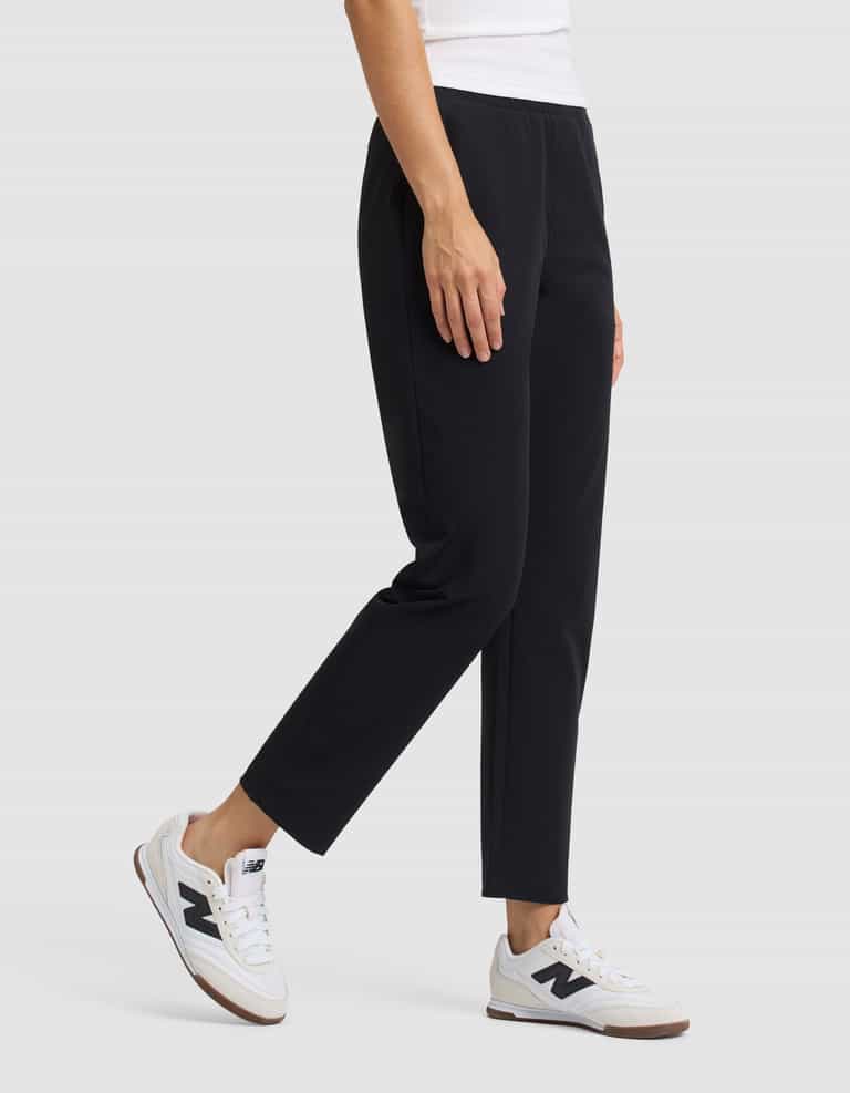 A person wearing Cozy Earth's Women's Always Cropped Pant in black, a white top, and white sneakers stands against a plain light gray background. Only the lower torso and legs are visible. |Color:Jet Black