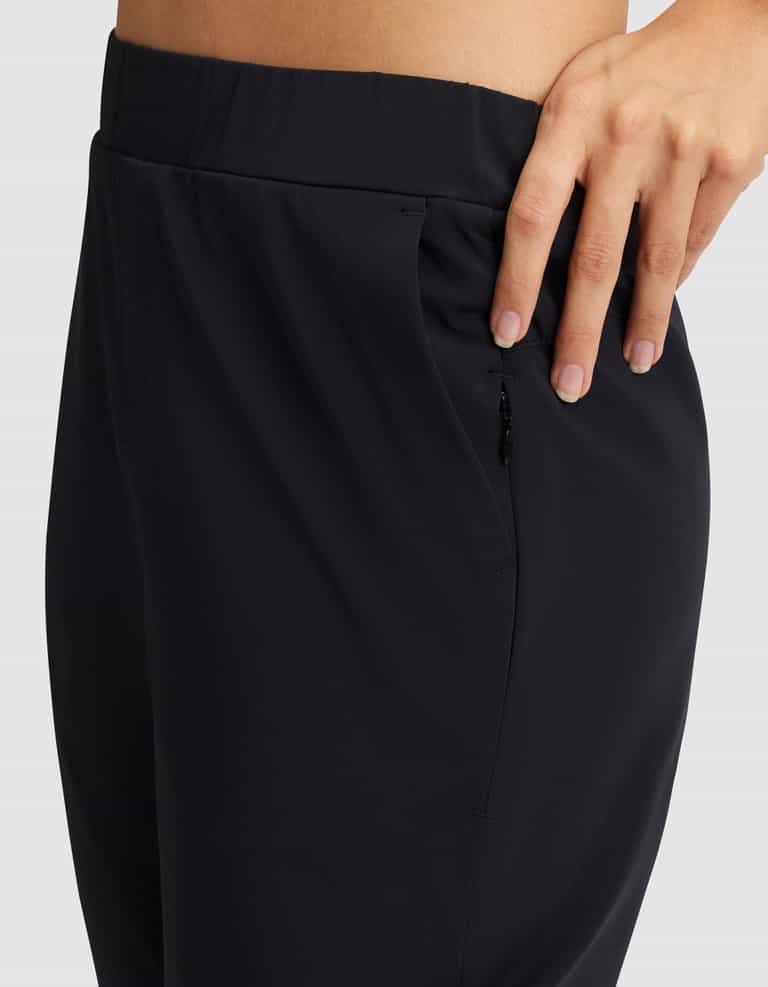 A close-up of a person wearing Cozy Earth's Women's Always Cropped Pant in black, featuring a zipper pocket and their hand resting on the waistband against a plain, light-colored background. |Color:Jet Black