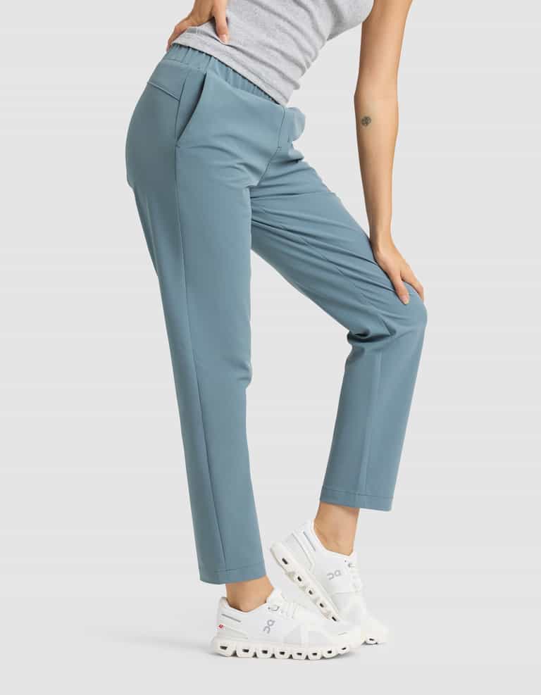 A person wearing Cozy Earth's Women's Always Cropped Pant in blue, paired with a grey sleeveless top and white sneakers, stands with one knee bent and a hand resting on their thigh. |Color:Oceanside