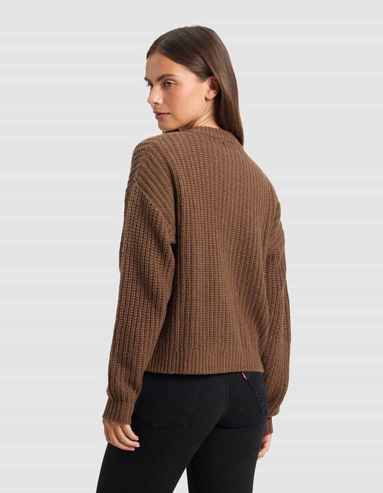A woman with long brown hair models the Cozy Earth Women's Arden Cardigan, standing against a plain light gray background and looking over her shoulder toward the camera.|Color:Cedar