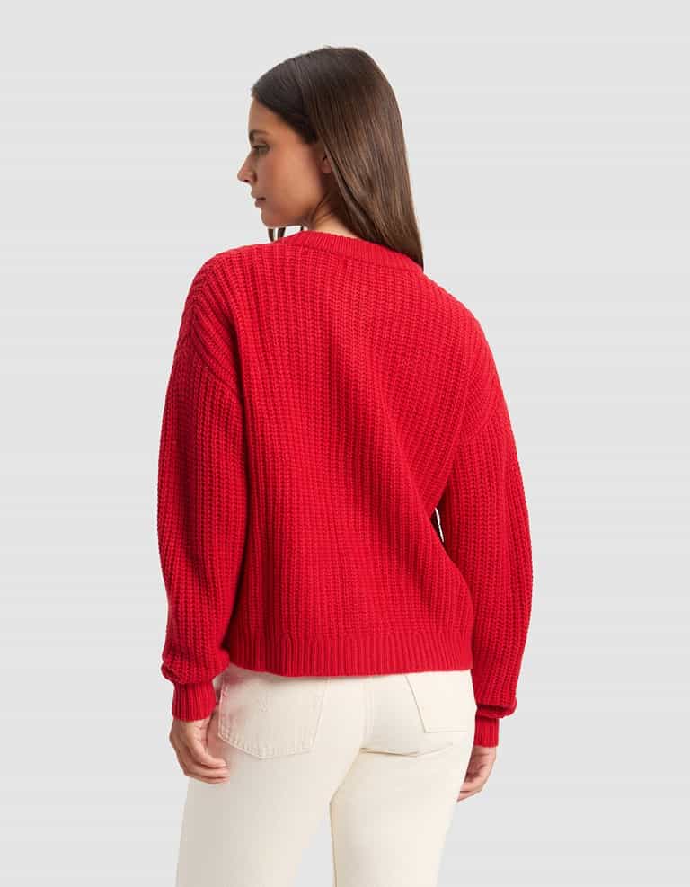 A woman with straight brown hair, seen from the back, models the Cozy Earth Women's Arden Cardigan in red and off-white pants against a plain light gray background, looking to the left.|Color:Crimson