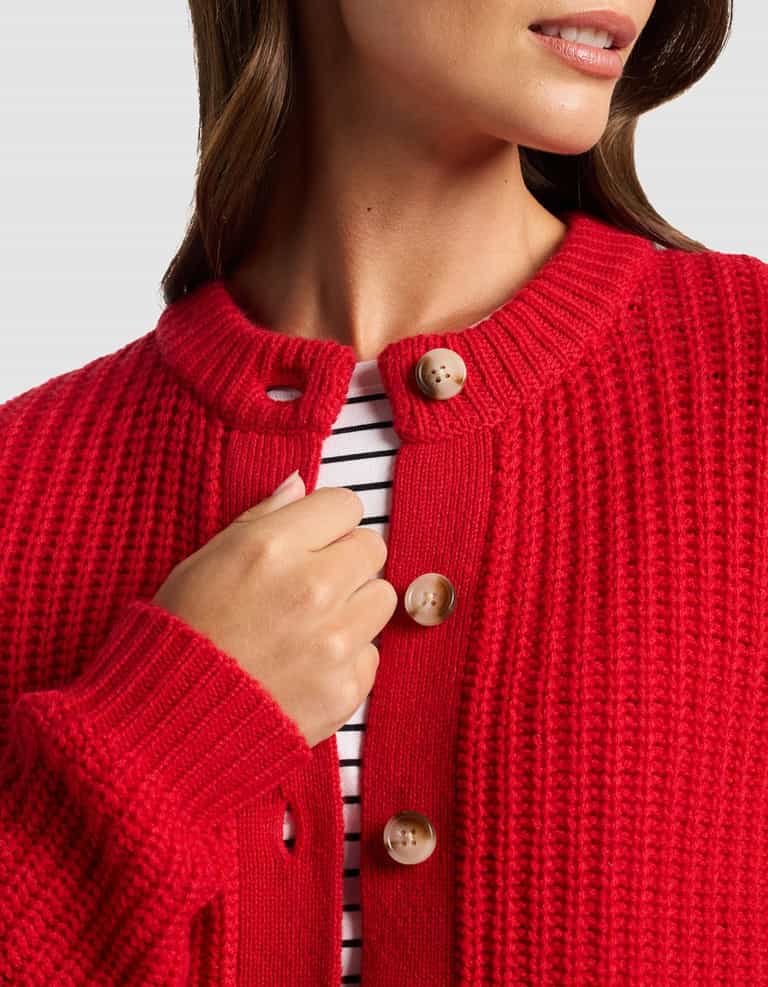 A woman wears the Cozy Earth Women's Arden Cardigan in textured red with tan buttons over a white and black striped shirt, shown from shoulders to mid-chest, with her hand near the collar.|Color:Crimson