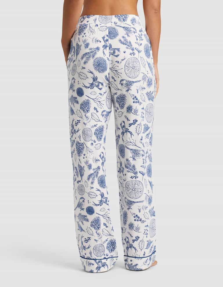 A person stands with their back to the camera wearing Cozy Earth Women's Bamboo Stretch-Knit Pajama Pant in white with a blue floral print. The pants are loose-fitting with pockets, showing only the lower back and legs against a plain background.|Color:Winter Toile Pacific