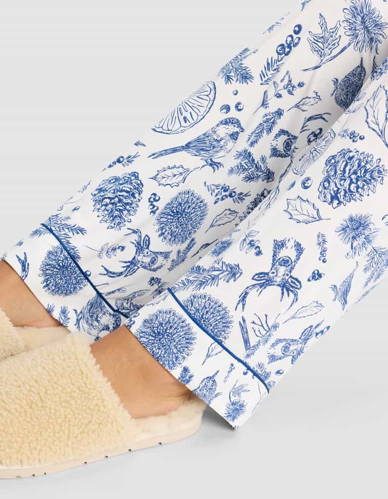 Close-up of a person wearing cream-colored slippers and Cozy Earth Women's Bamboo Stretch-Knit Pajama Pant, featuring a blue nature print with birds, leaves, pinecones, and acorns, set against a light background.|Color:Winter Toile Pacific