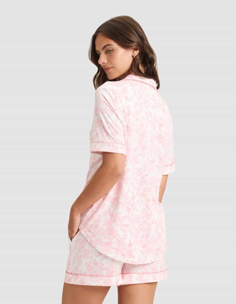 A woman stands with her hands in the pockets of her HIDE Women's Bamboo Stretch-Knit Short Sleeve Pajama Top and matching shorts, looking over her shoulder against a plain background. |Color:Tulip Toile