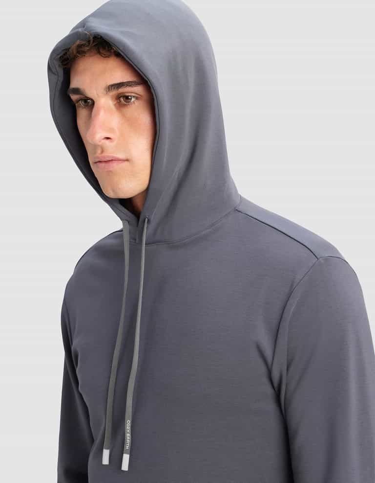A young man wears the Cozy Earth Men's Brushed Bamboo Hoodie in gray with the hood up, looking slightly to the side against a light gray background.|Color:Graphite